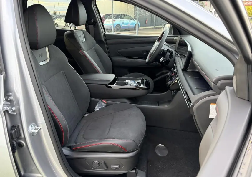 Vue intérieure côté conducteur du Hyundai Tucson 2025 argent métallisé avec sellerie N Line cuir/alcantara noire et surpiqûres rouges.