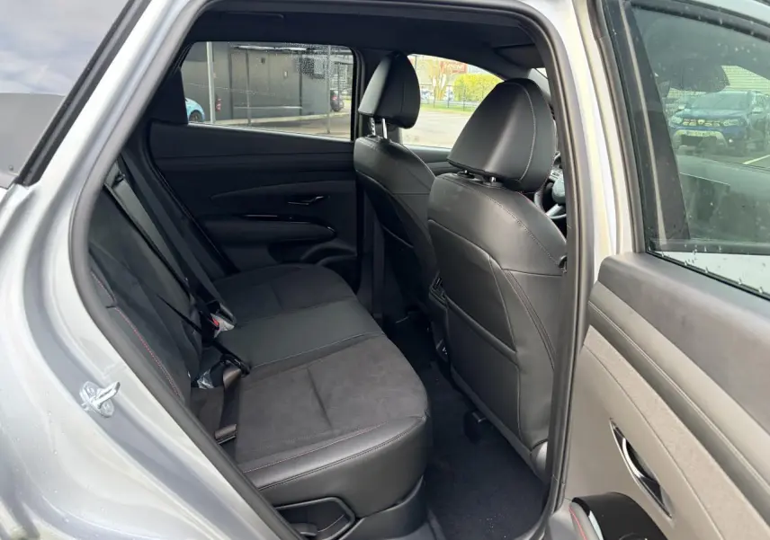 Vue intérieure arrière côté gauche du Hyundai Tucson 2025 gris métallisé, avec sellerie cuir/alcantara noire et surpiqûres rouges.