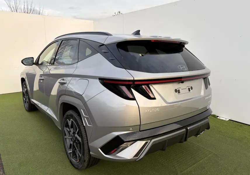 Vue 3/4 arrière gauche du Hyundai Tucson 2025 en gris métallisé avec feux arrière à LED et jantes alliage noires.