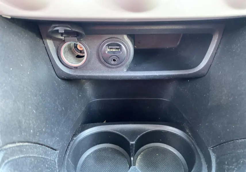 Prise 12V et port USB au-dessus des porte-gobelets noirs dans l’habitacle d’une Peugeot 208 gris foncé.