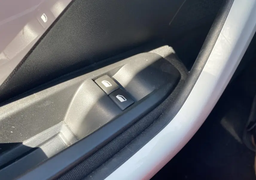 Gros plan sur les commandes des lève-vitres électriques côté conducteur d'une Peugeot 208 gris foncé.