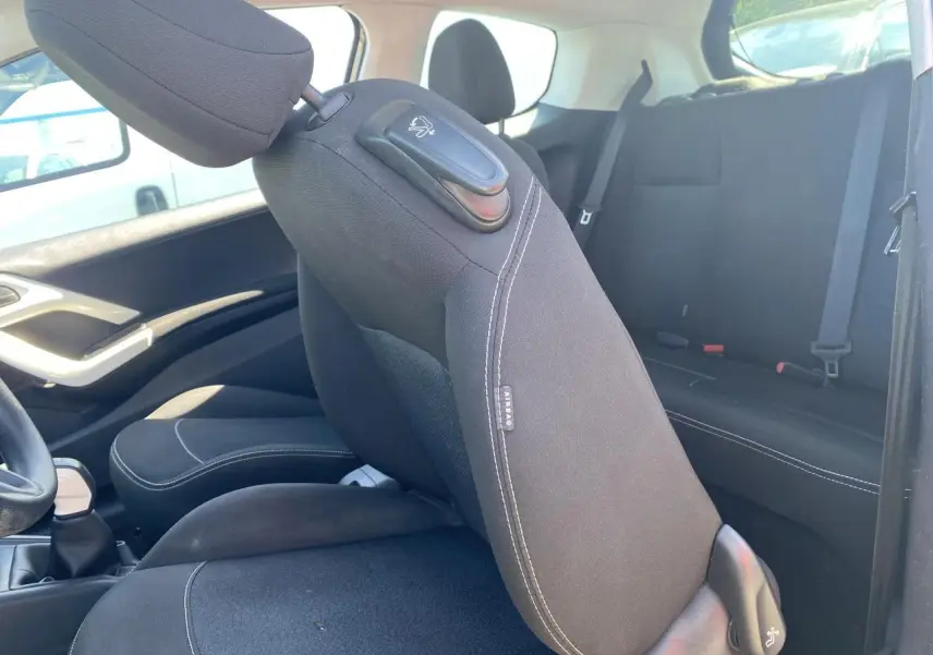 Vue intérieure côté gauche de la Peugeot 208 2018, sièges tissu noir avec surpiqûres blanches et dossier avant rabattable.