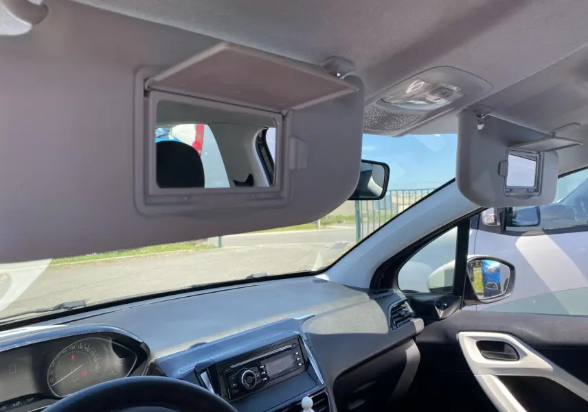 Intérieur Peugeot 208 2018 vu côté passager, tableau de bord gris avec pare-soleils ouverts et miroirs intégrés.