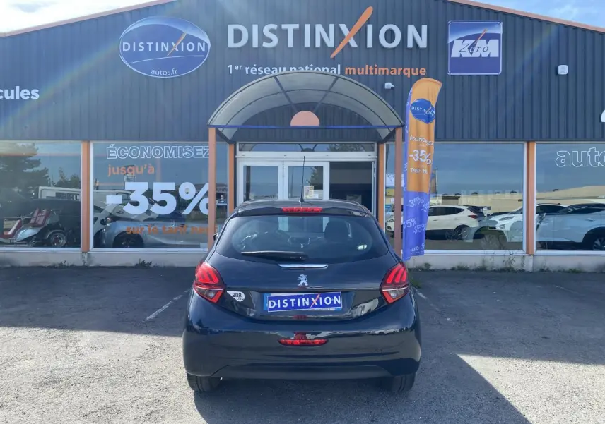 Vue arrière d'une Peugeot 208 gris foncé garée devant un showroom Distinxion avec plaques d'immatriculation publicitaires.