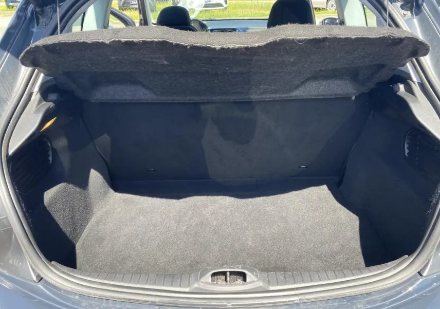 Coffre ouvert vu de l'arrière d'une Peugeot 208 gris foncé, montrant un espace de rangement propre et vide.