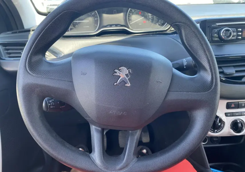 Vue rapprochée du volant noir avec logo Peugeot au centre, tableau de bord et console centrale en arrière-plan.