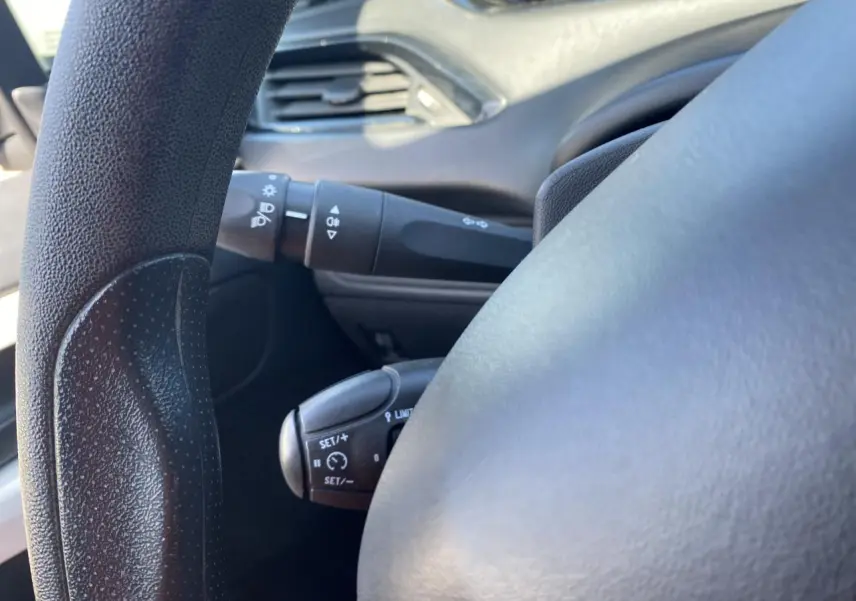 Gros plan sur le volant noir de la Peugeot 208 gris foncé, montrant les commandes du régulateur de vitesse côté gauche.