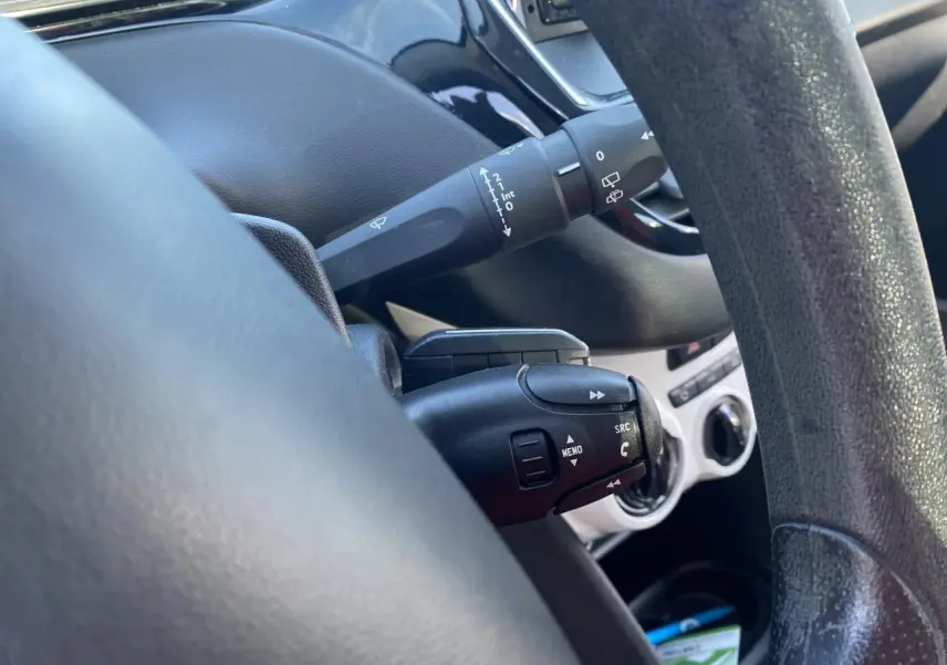 Gros plan sur la commande multifonction noire derrière le volant d’une Peugeot 208 gris foncé, intérieur épuré.