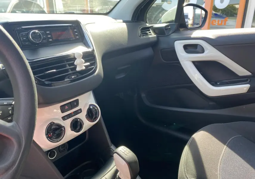 Vue intérieure côté passager de la Peugeot 208 2018, tableau de bord et console centrale avec détails blancs et levier de vitesse manuel.