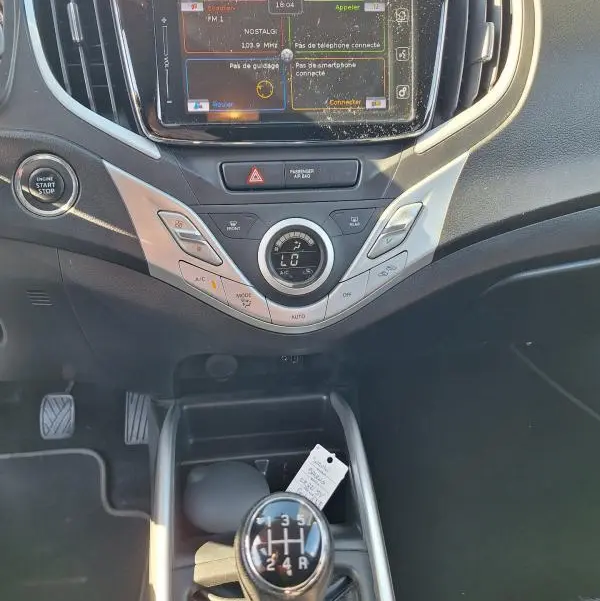 Vue intérieure centrée sur la console centrale et levier de vitesses manuelle d'une Suzuki Baleno gris clair de 2017.