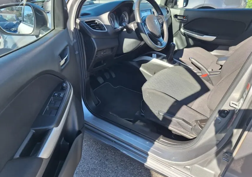 Intérieur côté conducteur de la Suzuki Baleno gris clair 2017, montrant le volant, la boîte manuelle et les sièges tissu.