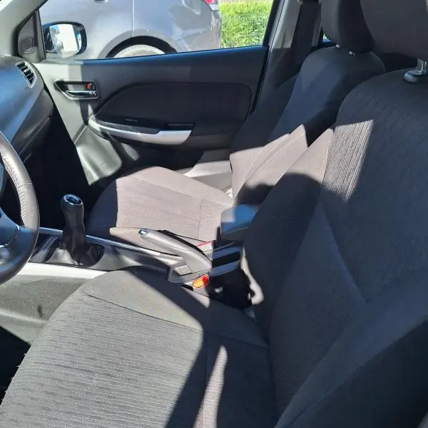 Vue intérieure côté conducteur de la Suzuki Baleno 1.0 Boosterjet Pack 2017, sièges tissu gris et levier de vitesses manuel visible.