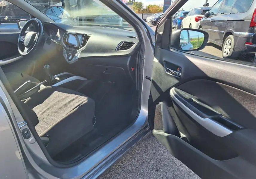 Intérieur côté conducteur gris clair de Suzuki Baleno 2017, montrant tableau de bord et boîte manuelle ouverte.