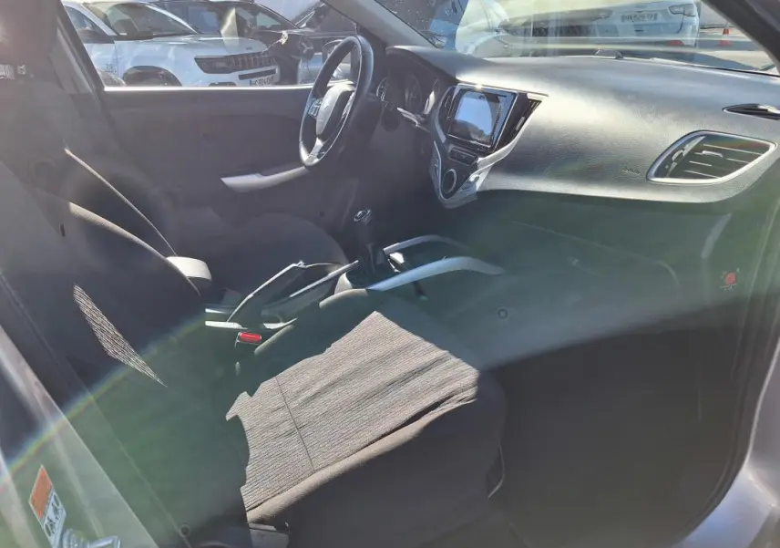Vue intérieure côté conducteur de la Suzuki Baleno gris clair, montrant le volant, la console centrale avec écran tactile et levier de vitesse manuel.