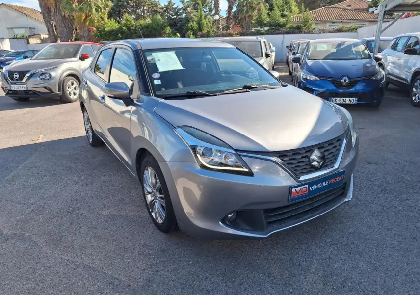 Vue 3/4 avant d'une Suzuki Baleno gris clair 2017 avec jantes alliage et phares xénon visibles.