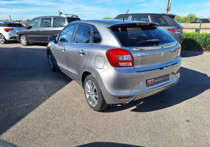 Vue 3/4 arrière droite d'une Suzuki Baleno gris clair avec vitres surteintées et jantes alliage 16 pouces.