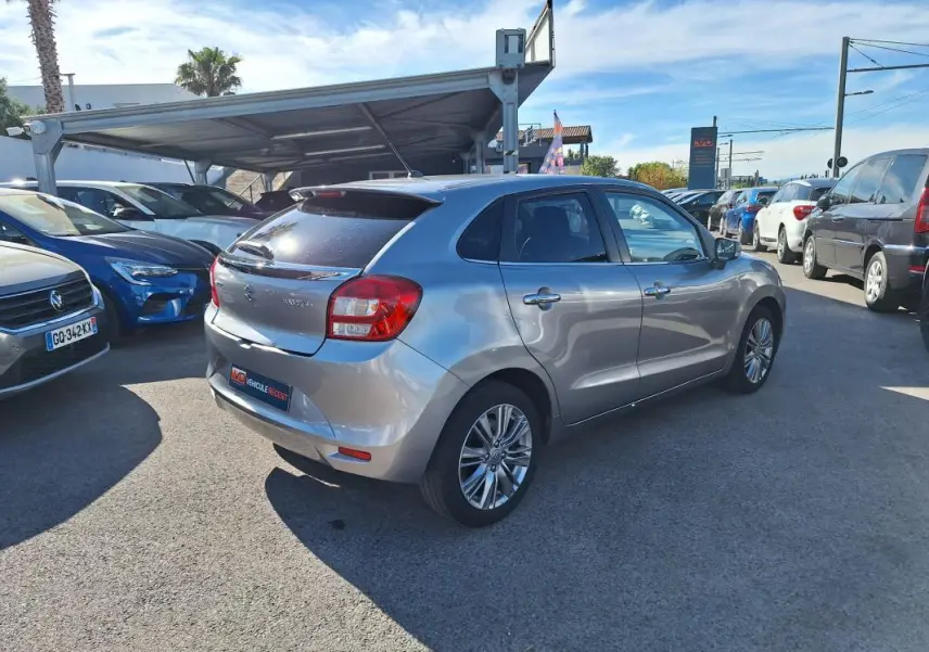 Vue 3/4 arrière droite d'une Suzuki Baleno gris clair avec jantes alliage 16 pouces, vitres surteintées et feux arrière visibles.