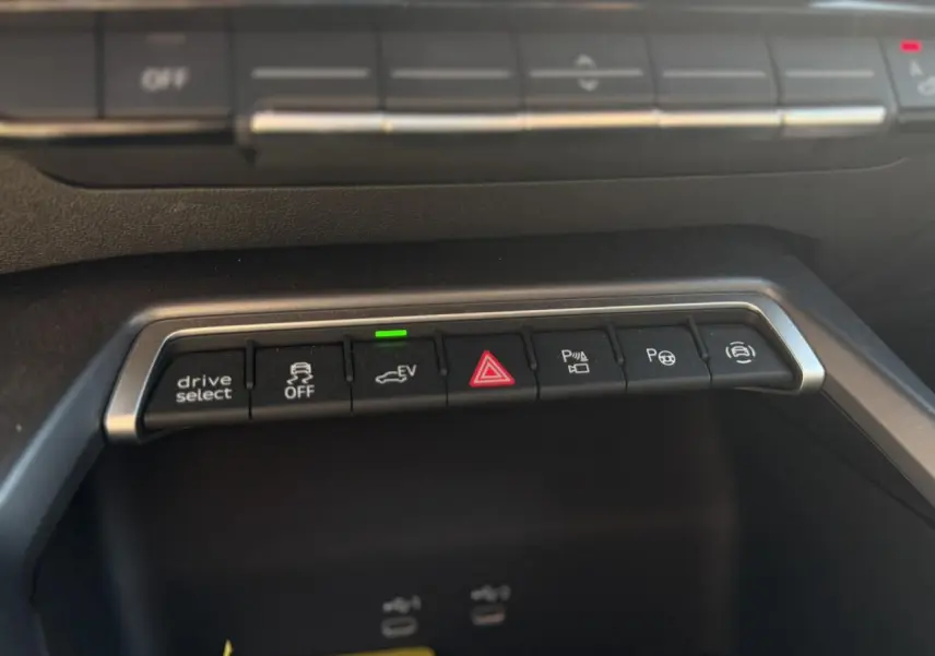 Gros plan sur la rangée de boutons de commande au centre de la console d'une Audi A3 Sportback noire, avec indicateur vert allumé.