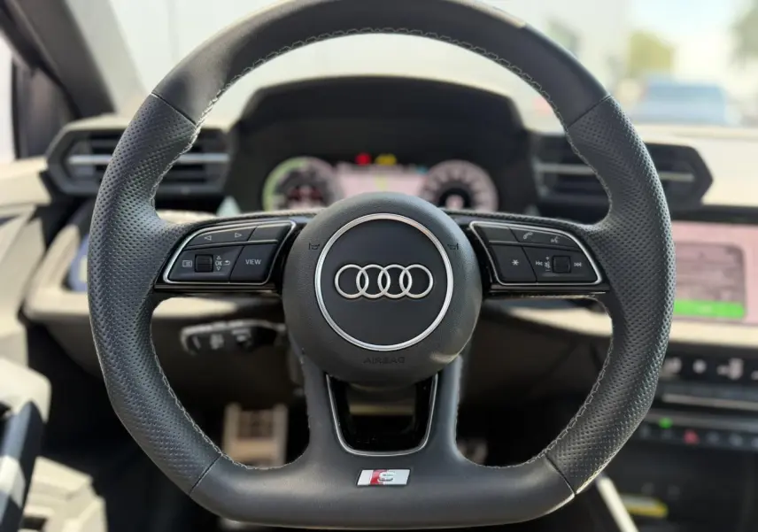 Volant cuir sport multifonctions Audi S-Line vu de face avec logo anneaux et commandes intégrées, intérieur noir.