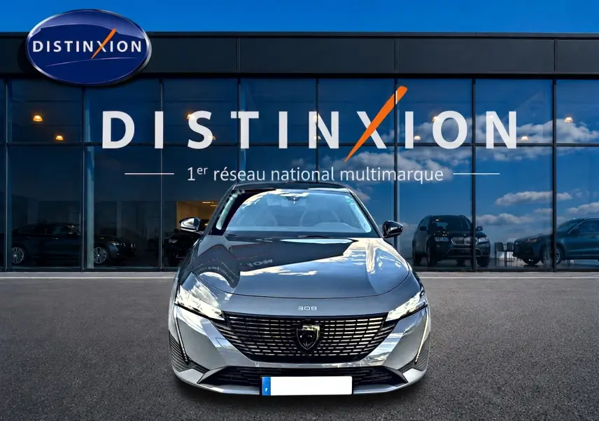 Vue avant d'une Peugeot 308 gris selenium garée devant une vitrine avec logo Distinxion.