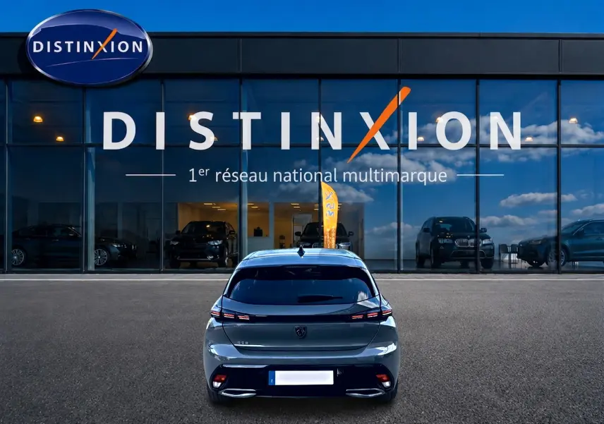 Vue arrière d'une Peugeot 308 gris selenium 2025 garée devant une vitrine avec logo Distinxion.