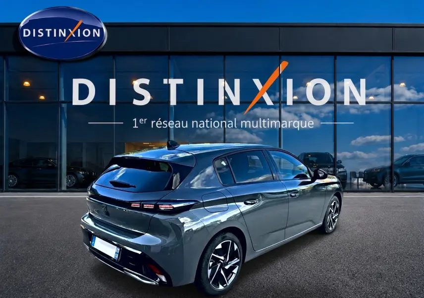 Vue 3/4 arrière droite d'une Peugeot 308 2025 gris selenium avec jantes alliage devant une vitrine Distinxion.