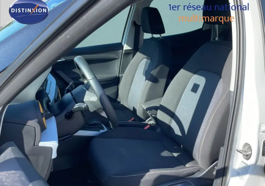 Vue intérieure côté conducteur du SEAT Arona blanc métal 2025, sièges tissu gris foncé avec inserts clairs.