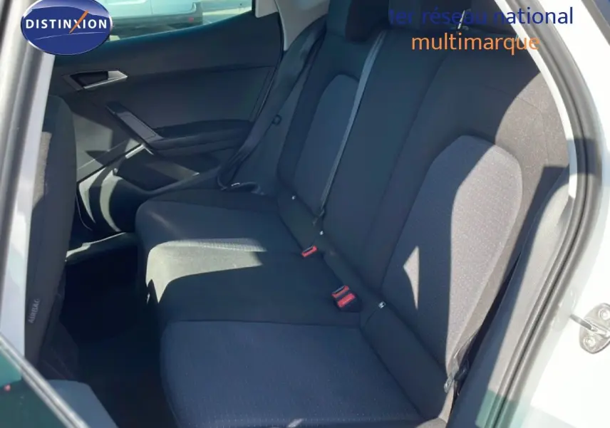 Vue intérieure des sièges arrière noirs d’un SEAT Arona blanc métal, avec ceinture de sécurité et porte arrière ouverte.