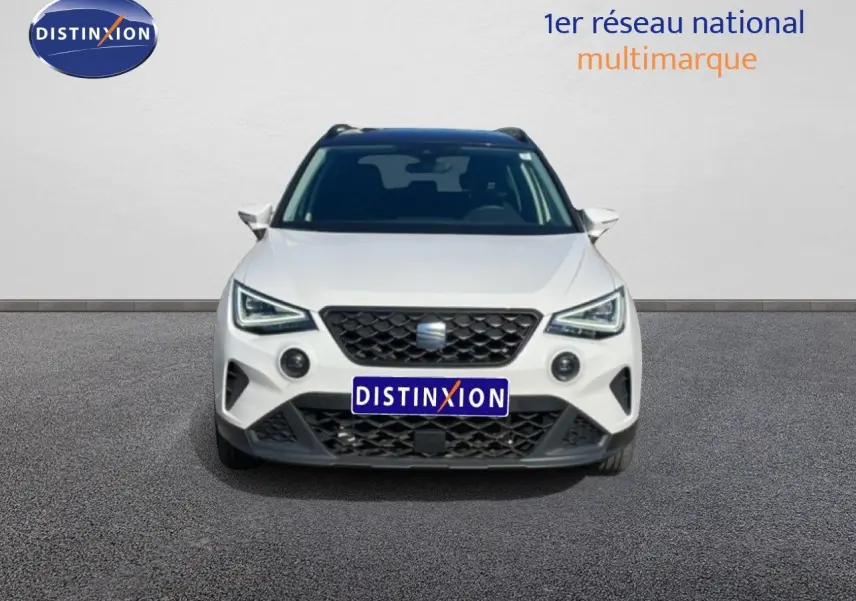 Vue frontale d'un SEAT Arona blanc métal avec toit noir, calandre noire et feux LED anguleux visibles.
