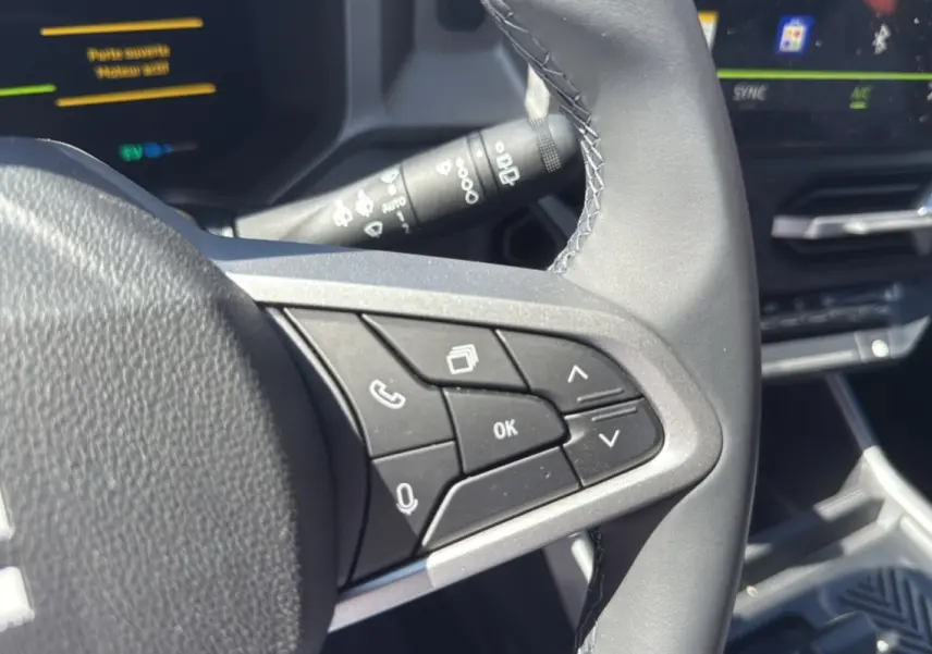 Gros plan sur les commandes au volant cuir noir du Dacia Bigster Hybrid 150 4x4, avec tableau de bord digital en arrière-plan.