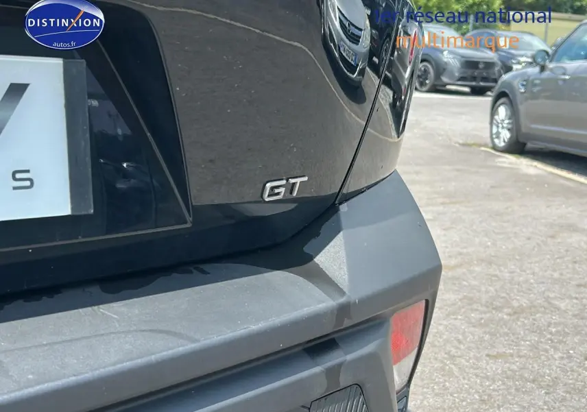 Gros plan sur le logo GT à l'arrière droit d'une Peugeot 408 Hybrid 145 GT noire 2024 en extérieur.