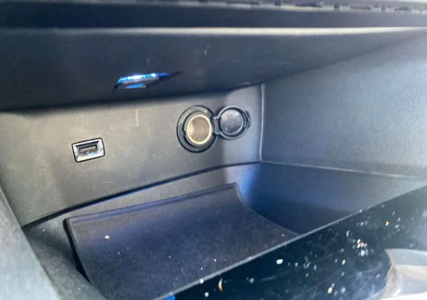 Prise allume-cigare et port USB dans le rangement central d'un Peugeot 3008 2019, intérieur noir.