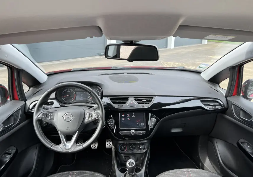 Vue intérieure avant de l'Opel Corsa rouge avec tableau de bord noir brillant et volant multifonctions cuir.