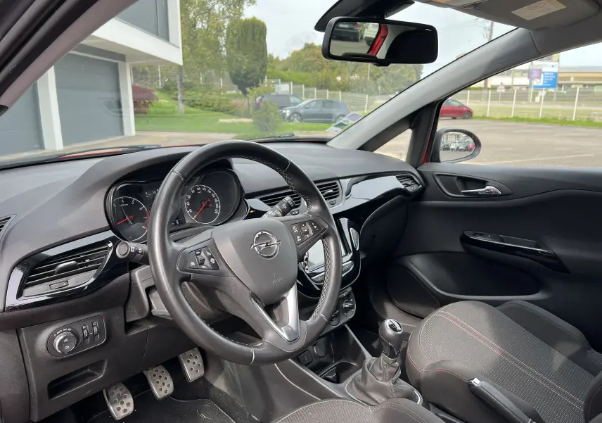 Vue intérieure côté conducteur de l'Opel Corsa rouge 2018, volant cuir multifonctions et levier de vitesses manuel.