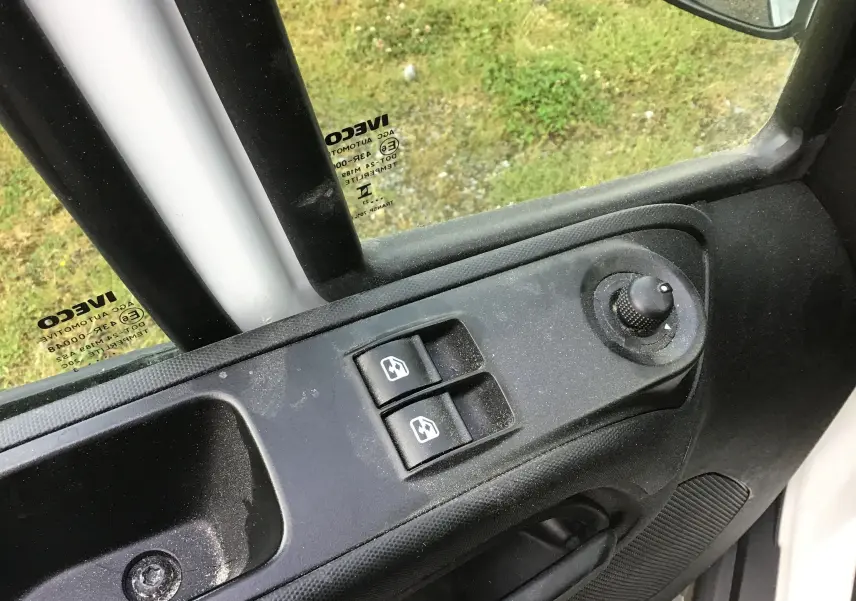 Vue rapprochée de la commande des vitres électriques et du réglage des rétroviseurs côté conducteur du fourgon Iveco Daily blanc 2023.