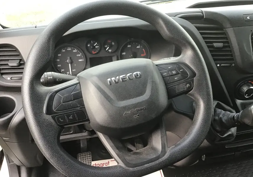 Vue rapprochée du volant noir d’un Iveco Daily Fourgon 2023 avec tableau de bord et levier de vitesses manuelle visibles.