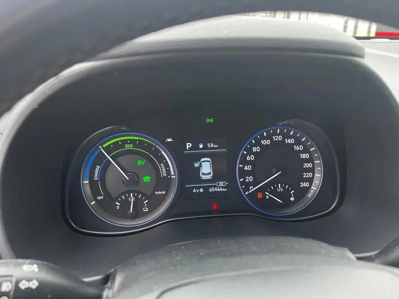 Vue rapprochée du tableau de bord numérique du Hyundai Kona bleu, affichant la vitesse, autonomie et indicateurs hybrides.