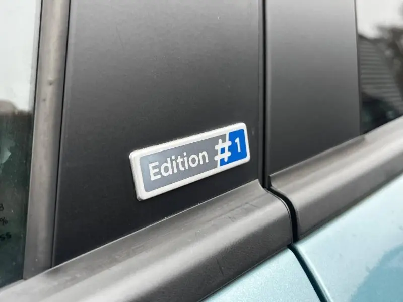 Gros plan sur l'écusson Edition 1 en bleu et blanc sur la porte côté gauche d'un Hyundai Kona bleu.