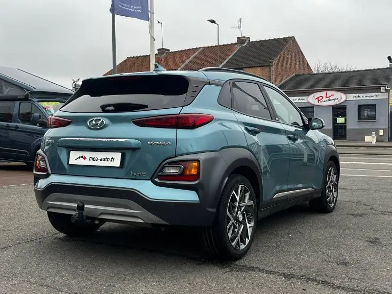Vue 3/4 arrière droite d'un Hyundai Kona hybride bleu avec jantes alu et attelage de remorque visible.
