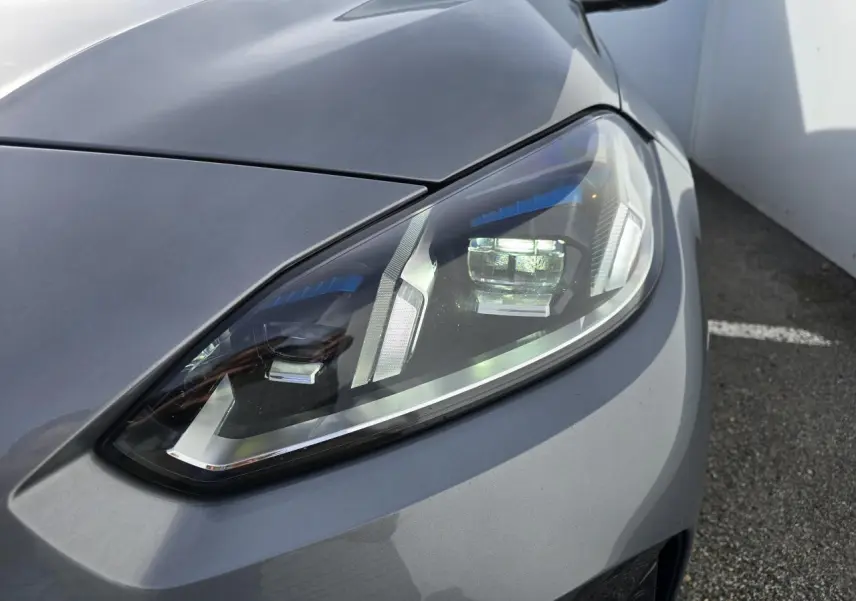 Gros plan sur le phare avant droit de la BMW Série 1 gris Skyscraper avec détails LED et toit noir visible en arrière-plan.