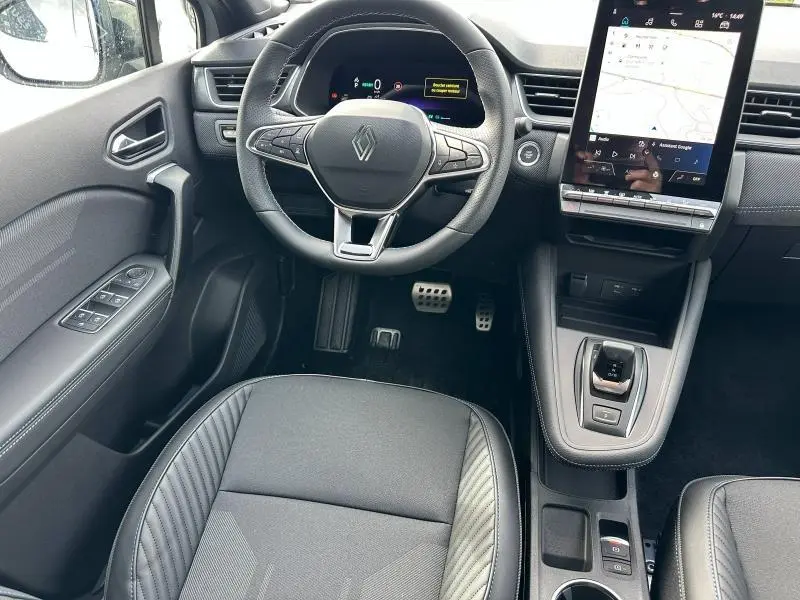 Vue intérieure avant du Renault Captur 2026 hybride, tableau de bord noir avec écran tactile vertical et volant multifonction.