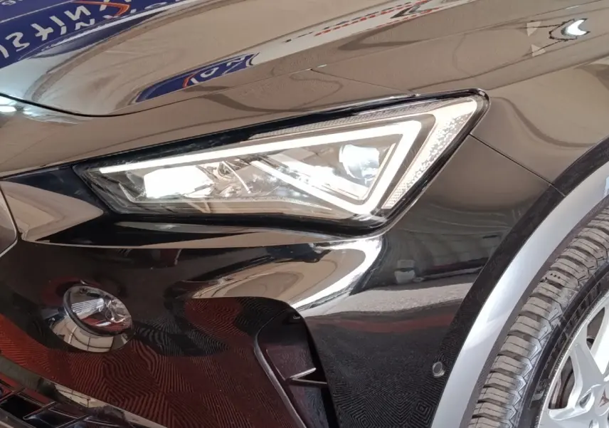 Gros plan sur le phare avant gauche noir brillant du CUPRA Formentor 2024 avec jante et capteur de stationnement visible.