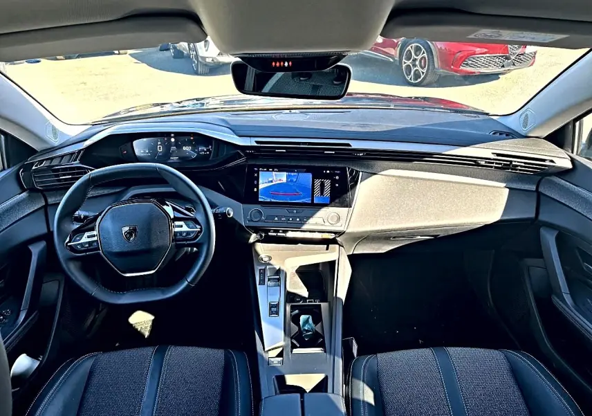 Vue intérieure avant de la Peugeot 308 noire 2025, avec tableau de bord numérique et écran tactile central allumé.