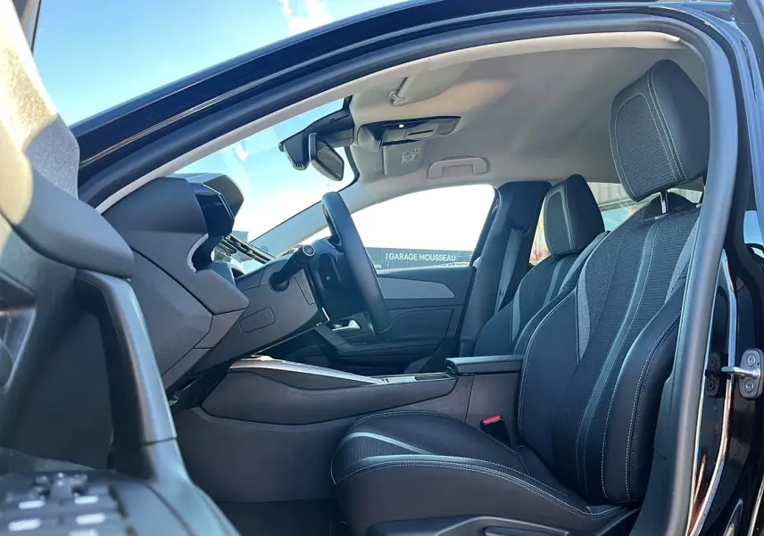 Vue intérieure côté conducteur d'une Peugeot 308 noire 2025, mettant en valeur les sièges et l'accoudoir central.