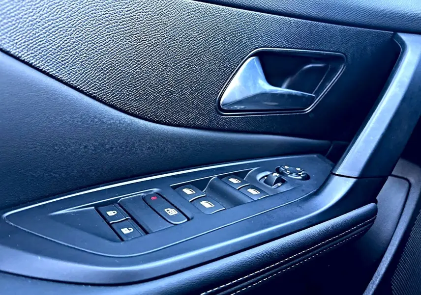 Gros plan sur la commande des vitres et la poignée intérieure côté conducteur de la Peugeot 308 noire, finition Allure.