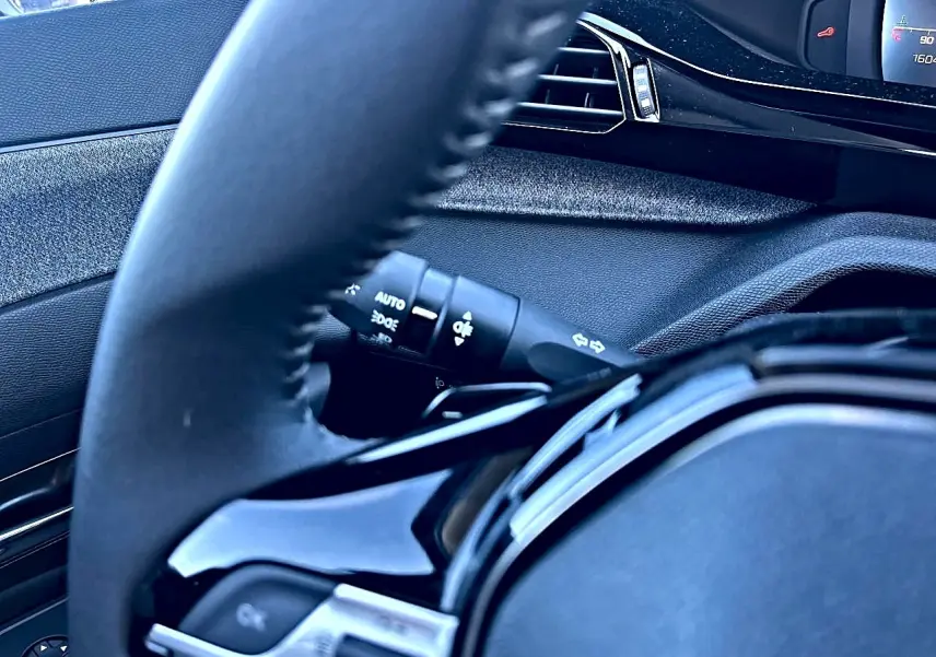 Gros plan sur le volant noir et la commande des phares d'une Peugeot 308 2025, intérieur moderne et épuré.