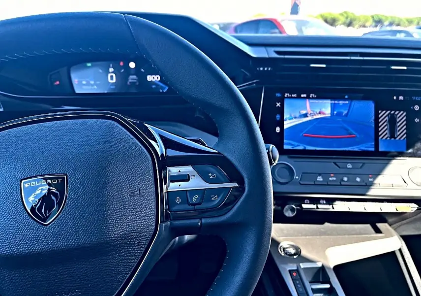 Vue intérieure centrée sur le volant noir Peugeot et l'écran tactile affichant la caméra de recul de la 308 2025.