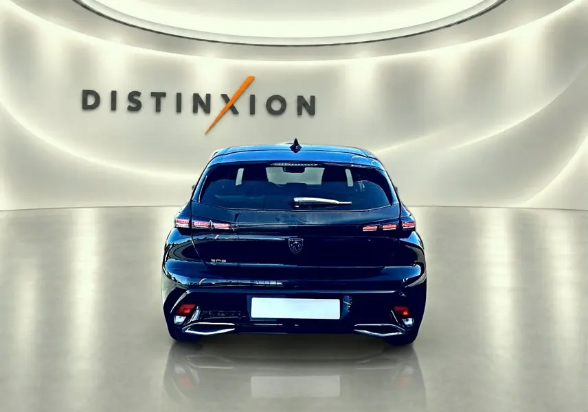 Vue arrière d'une Peugeot 308 noire 2025 avec feux LED et logo distinctif dans un showroom lumineux.