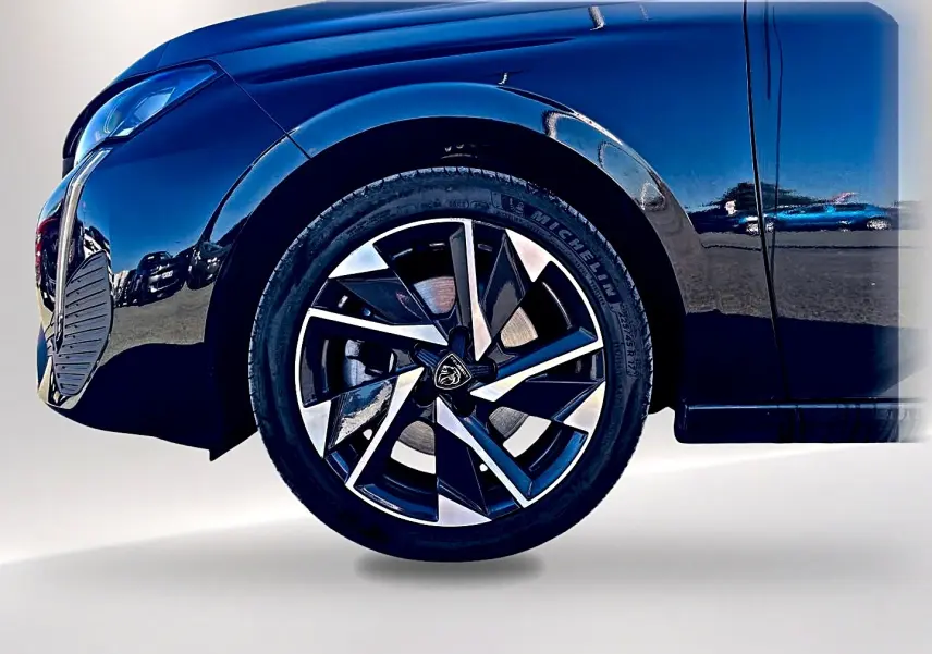Gros plan sur la roue avant gauche et la jante alu noire et argentée d'une Peugeot 308 noire 2025.