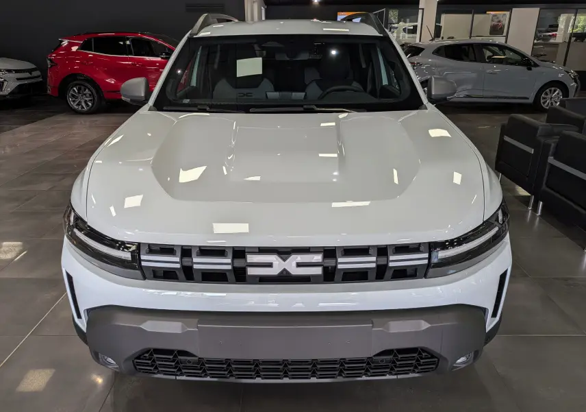 Vue frontale d'un Dacia Duster Hybrid-G blanc Glacier, avec calandre noire distinctive et pare-chocs robuste en showroom.